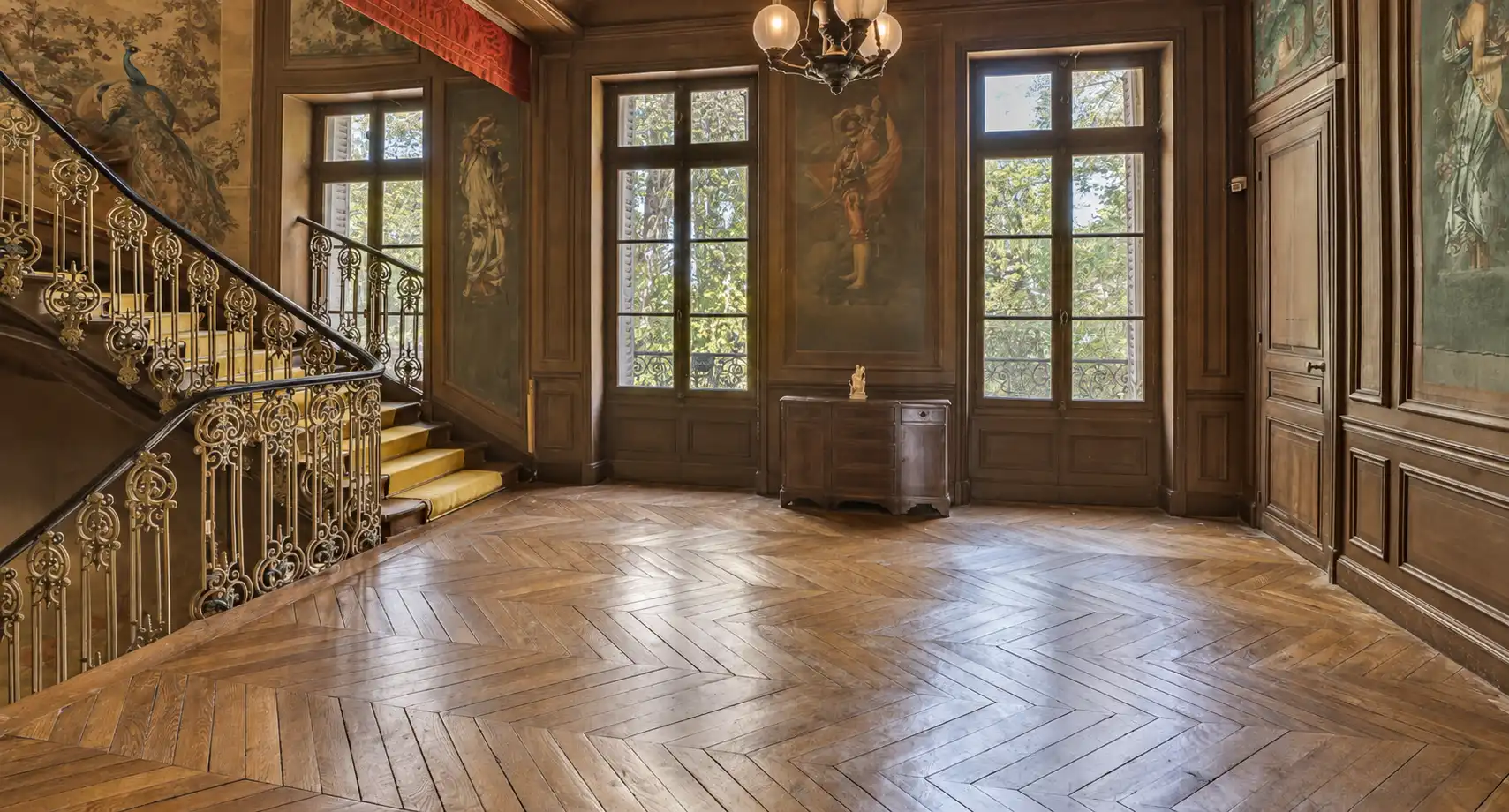 Grand palier au parquet ancien, lustre, hautes portes-fenêtres et rampe dorée