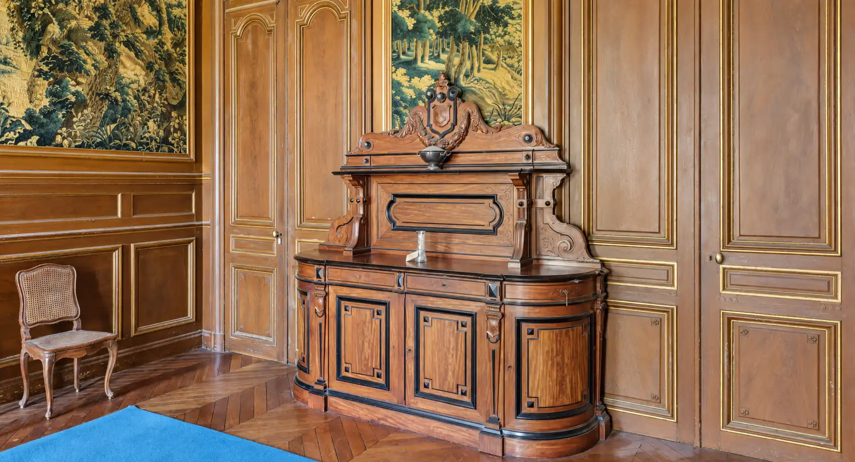 Buffet en bois sculpté à miroir devant des boiseries de chêne et une tapisserie