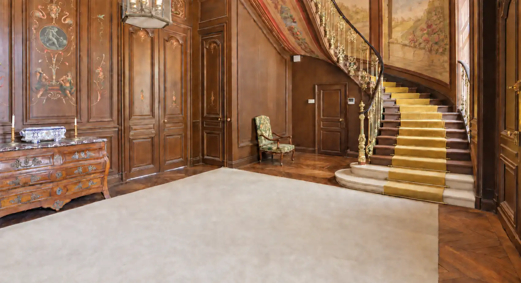 Vestibule lambrissé avec commode ancienne, tapis clair et départ d'escalier à tapis rouge