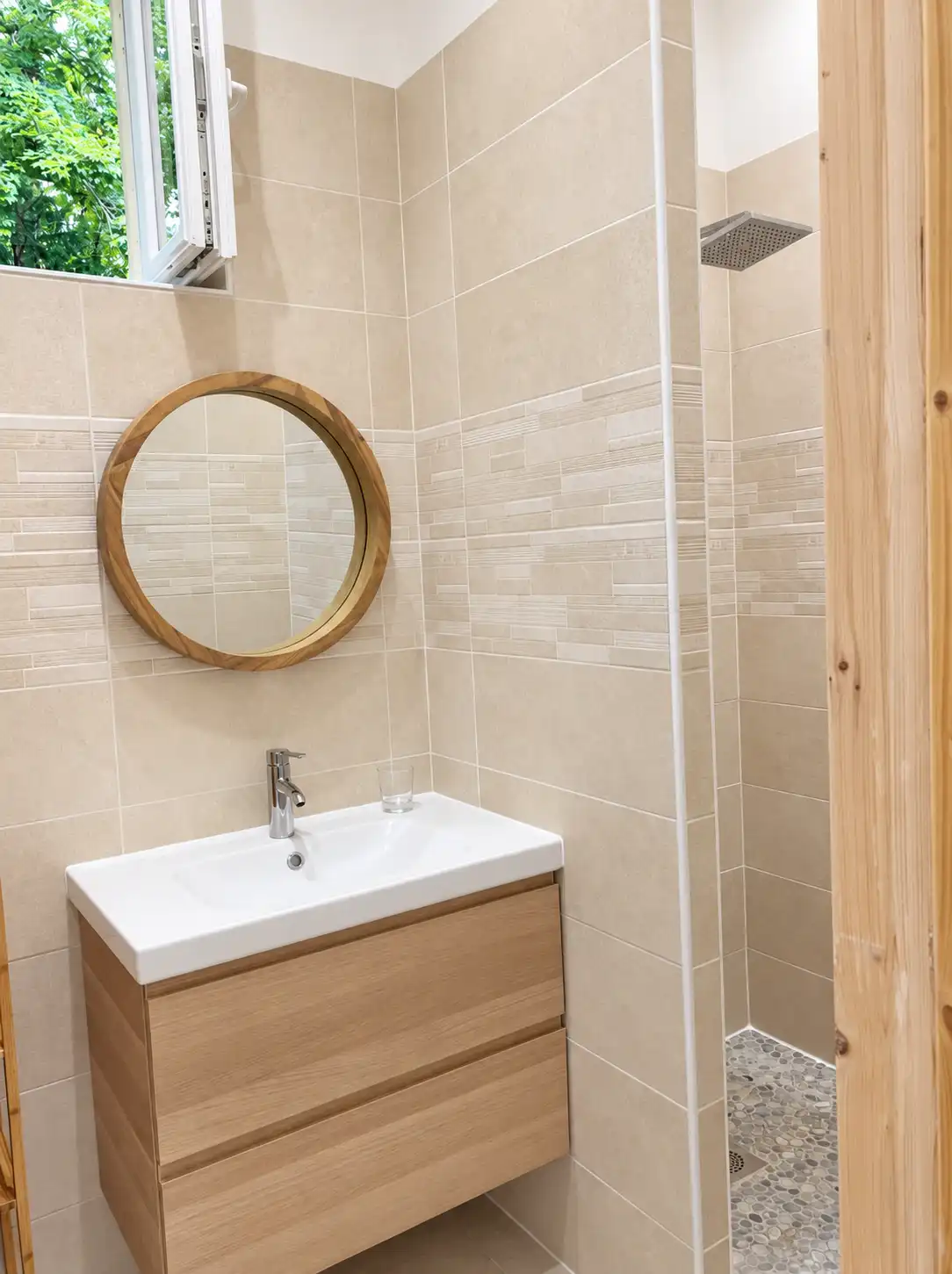 Meuble vasque en bois clair, miroir rond et douche à l'italienne carrelée de beige