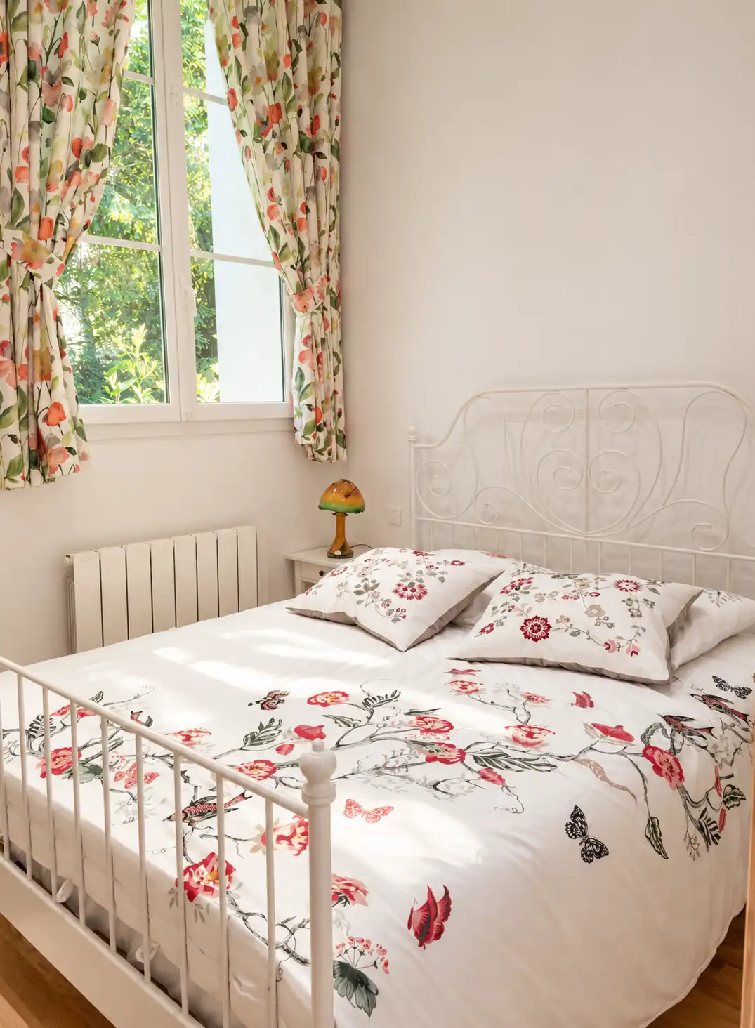 Chambre du Bon Espoir avec lit en fer forgé blanc, parure fleurie et rideaux assortis