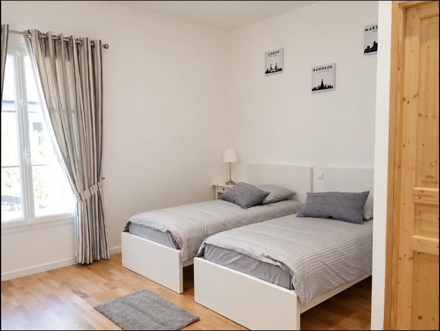 Deux lits simples gris et blancs, rideaux clairs et parquet dans la première chambre du Bon Espoir