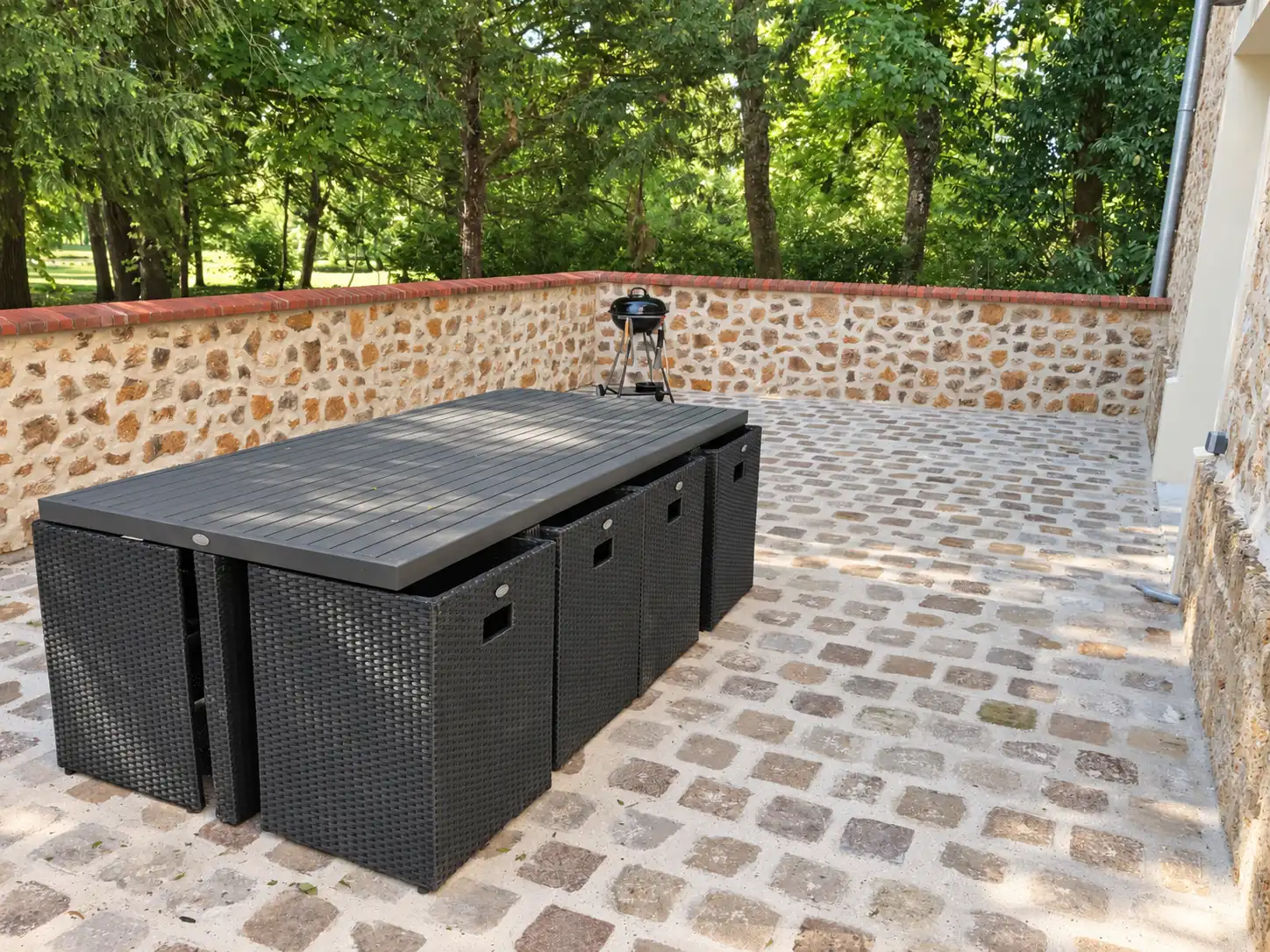 Terrasse pavée du Bon Espoir close de murs en pierre, avec salon de jardin noir et barbecue