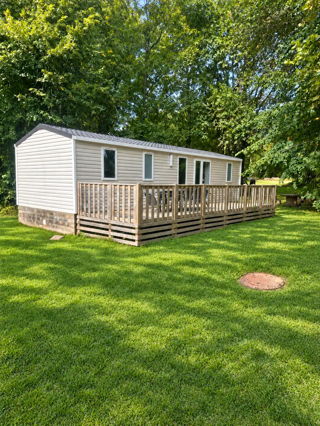 Le Bungalow et sa terrasse en bois sur la pelouse, entourés de grands arbres