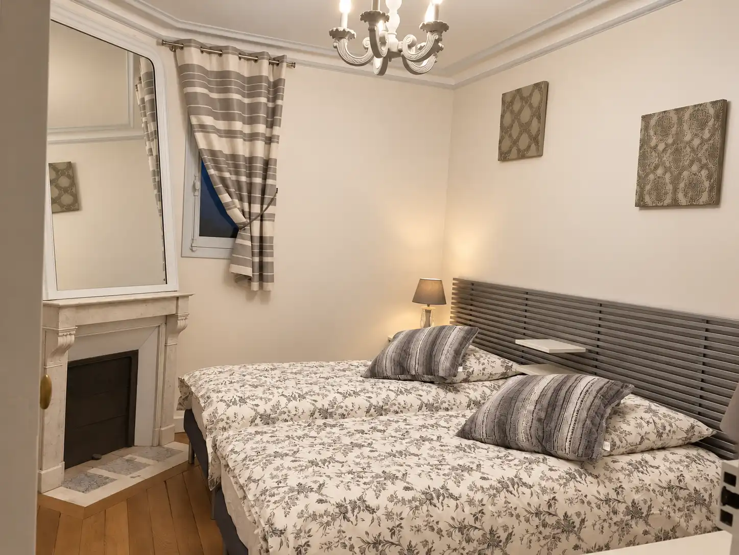 Deux lits simples aux parures fleuries, tête de lit grise et cheminée dans une chambre du Gardien