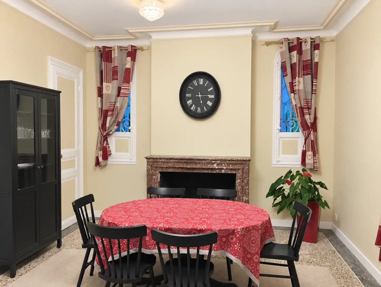Table ovale nappée de rouge et chaises noires devant la cheminée de la salle à manger du Gardien