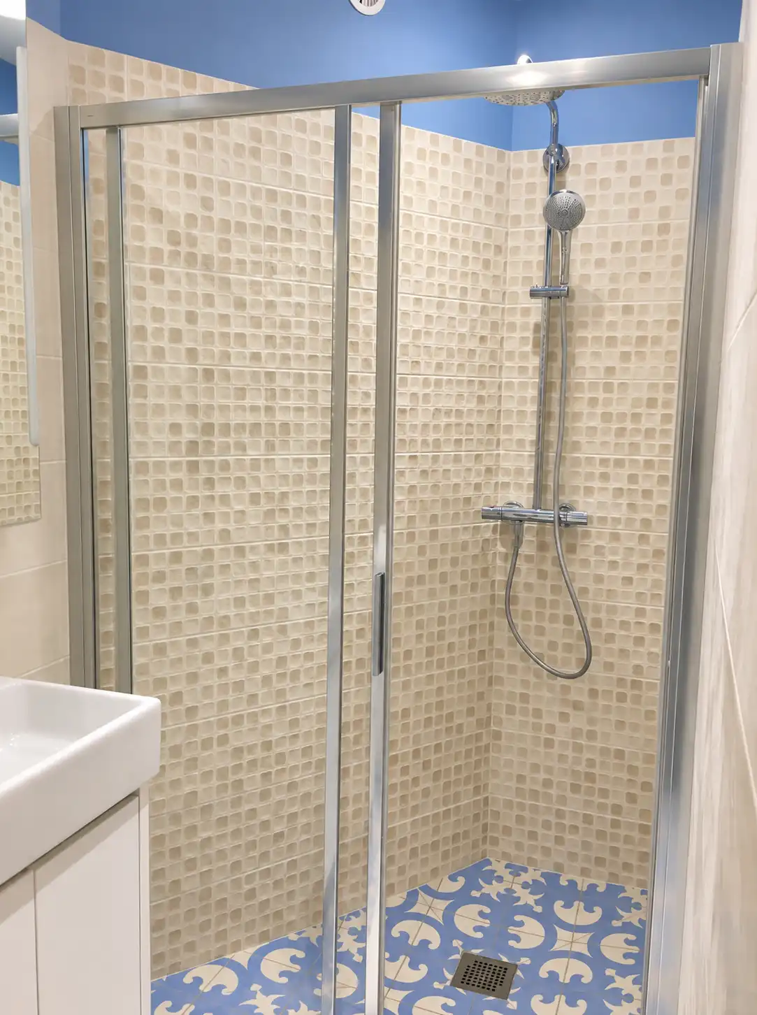 Cabine de douche carrelée de mosaïque beige et sol en carreaux bleus au Gardien