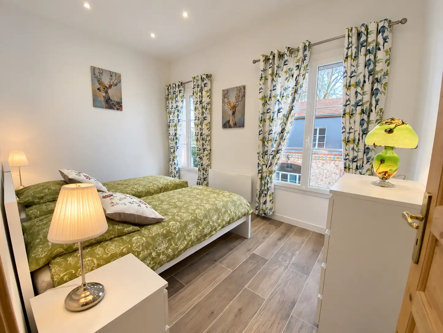Chambre du Monarque au couvre-lit vert, rideaux fleuris et fenêtre ouverte sur les arbres