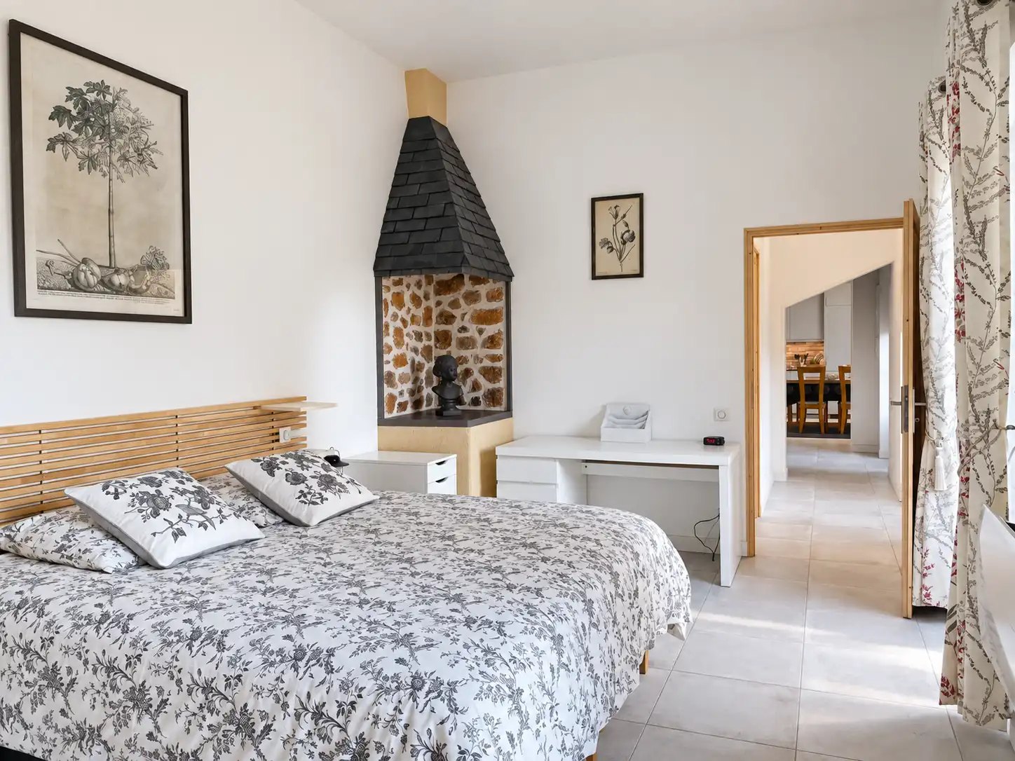 Chambre du rez-de-chaussée du Monarque avec grand lit, cheminée en pierre et gravures botaniques