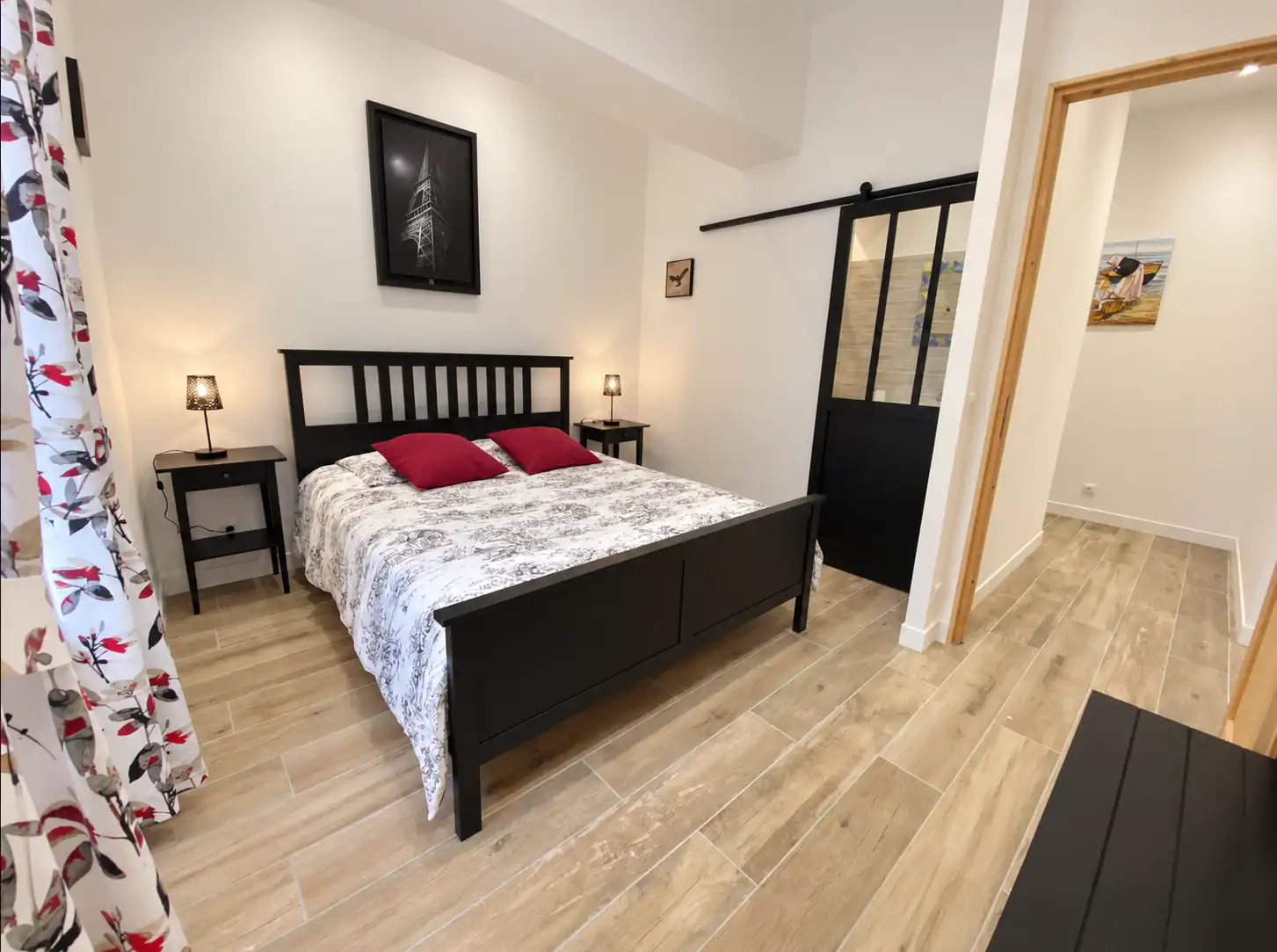 Chambre du Monarque avec lit en bois noir, coussins rouges et porte coulissante vitrée noire