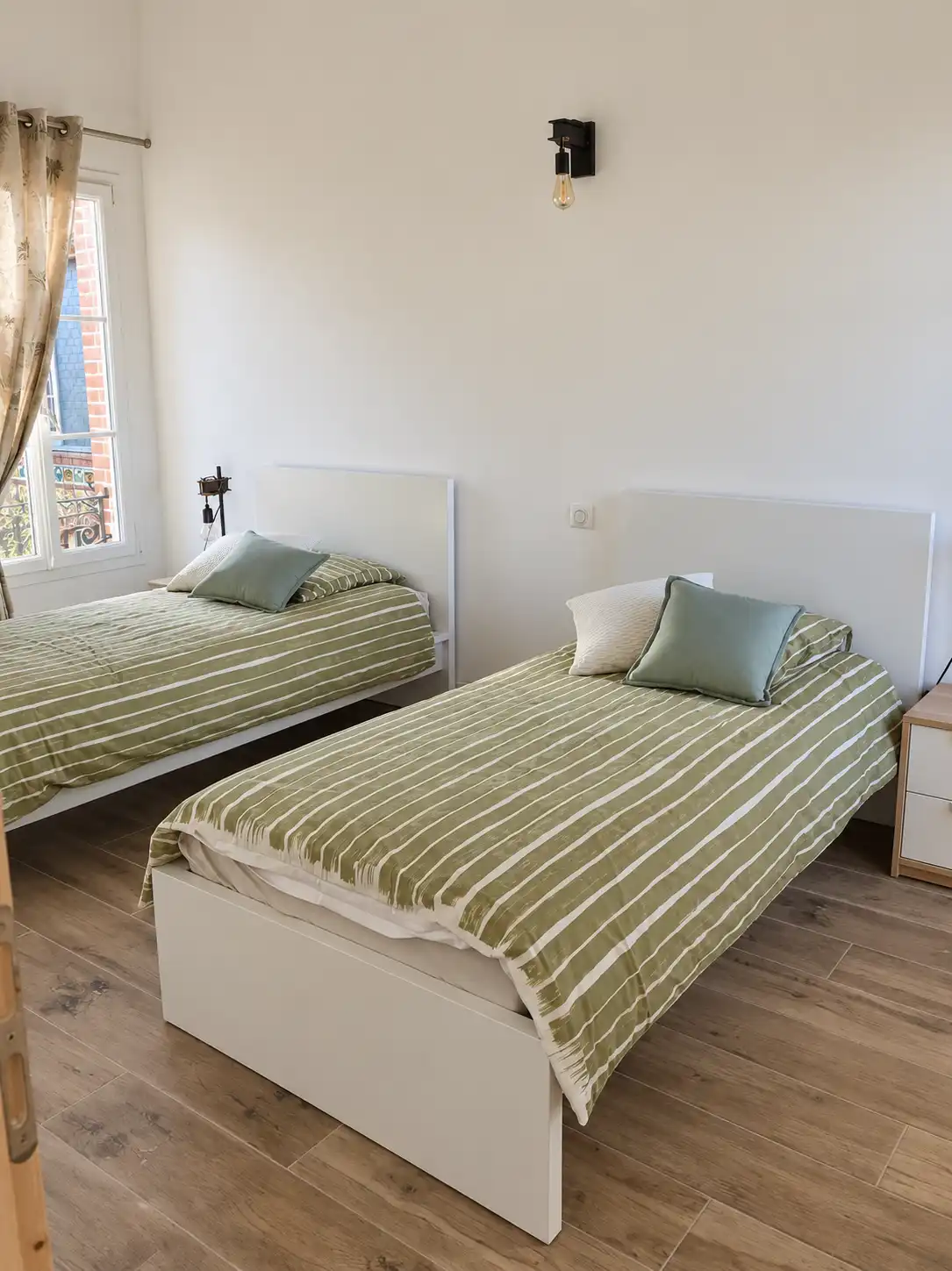 Deux lits simples aux couvre-lits verts rayés dans une chambre claire du Monarque