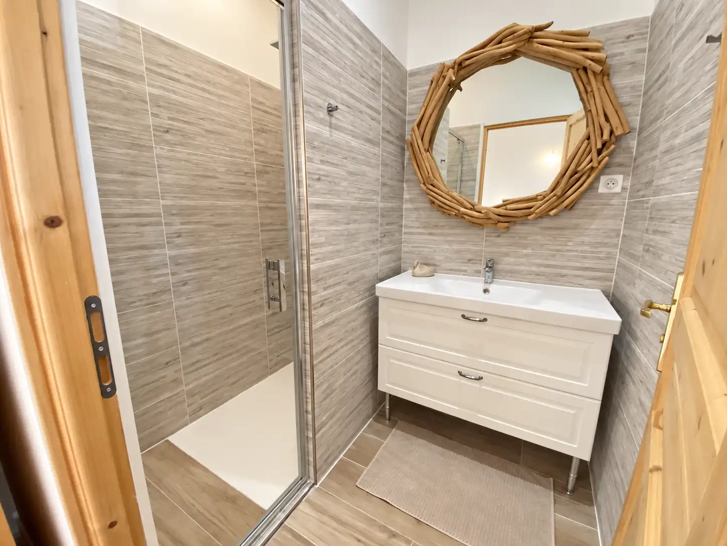 Salle d'eau du Monarque avec cabine de douche vitrée et miroir rond cerclé de bois flotté