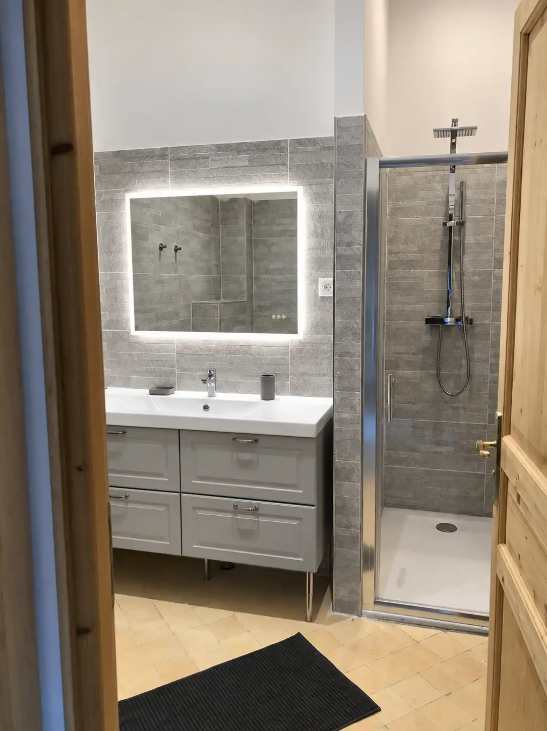 Meuble vasque gris surmonté d'un miroir rétroéclairé, cabine de douche à droite, au Monarque