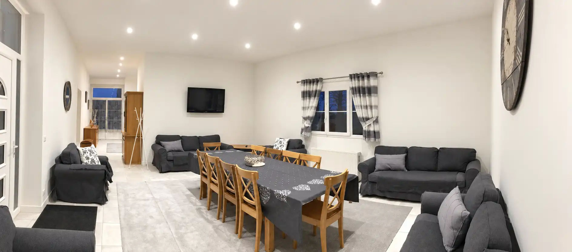 Grande pièce à vivre du Monarque avec canapés gris, longue table et télévision murale