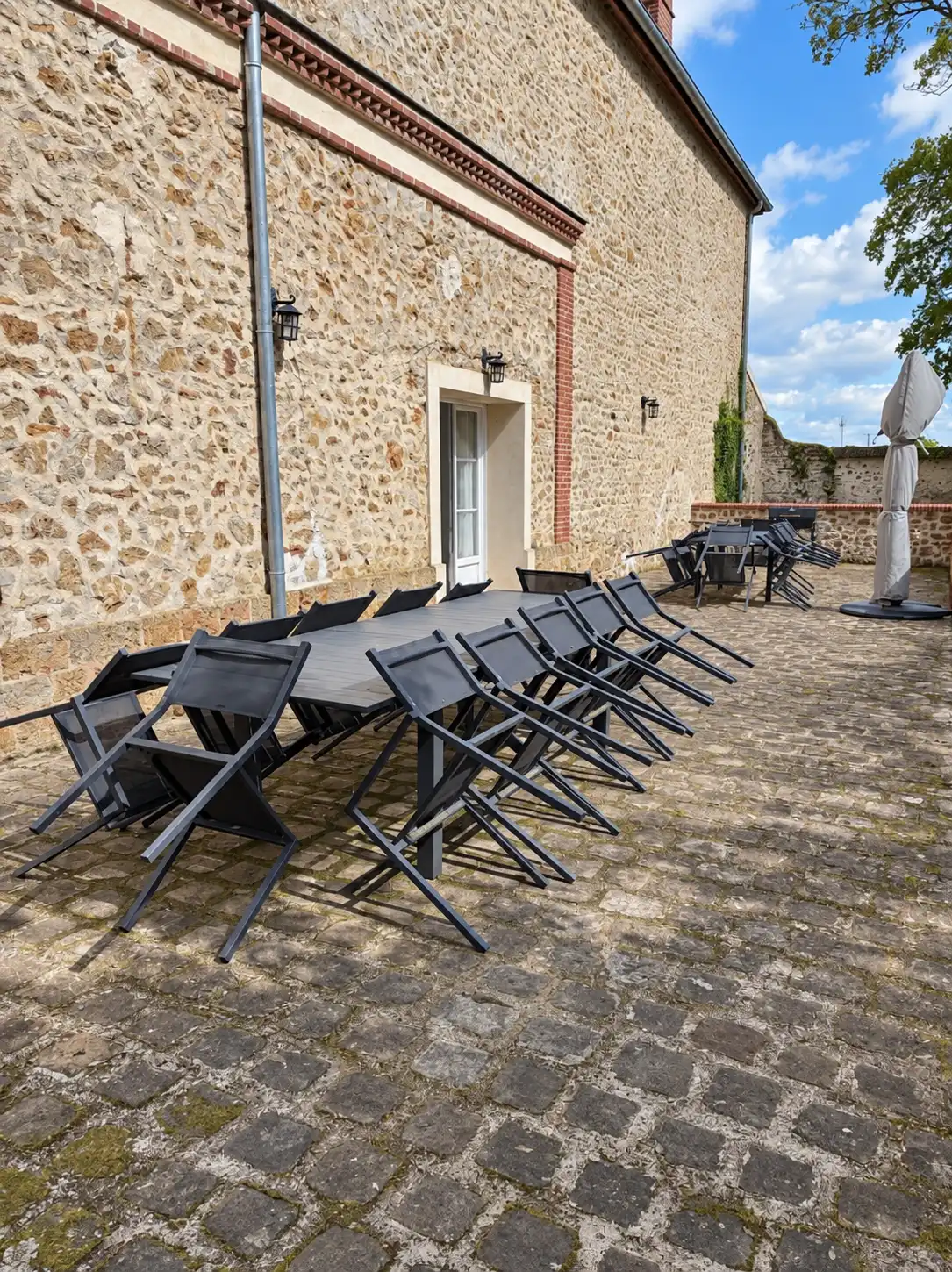 Terrasse pavée du Monarque le long du mur en pierre, avec tables et chaises pliantes noires