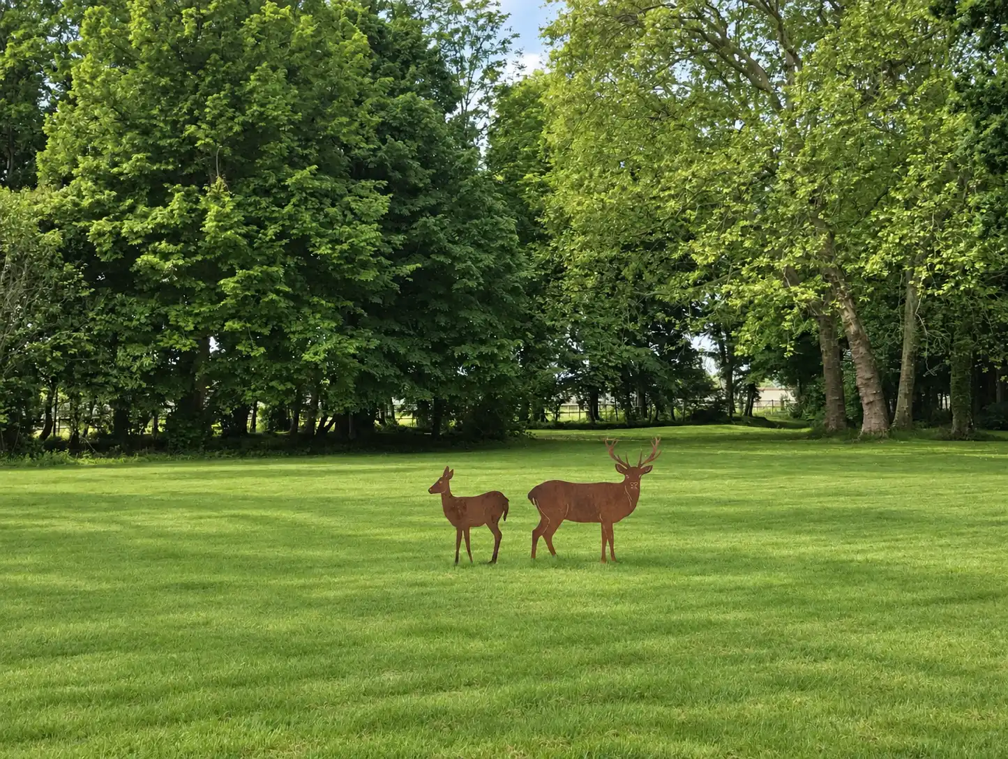 Deux silhouettes de cerfs en métal rouillé sur une pelouse bordée d'arbres
