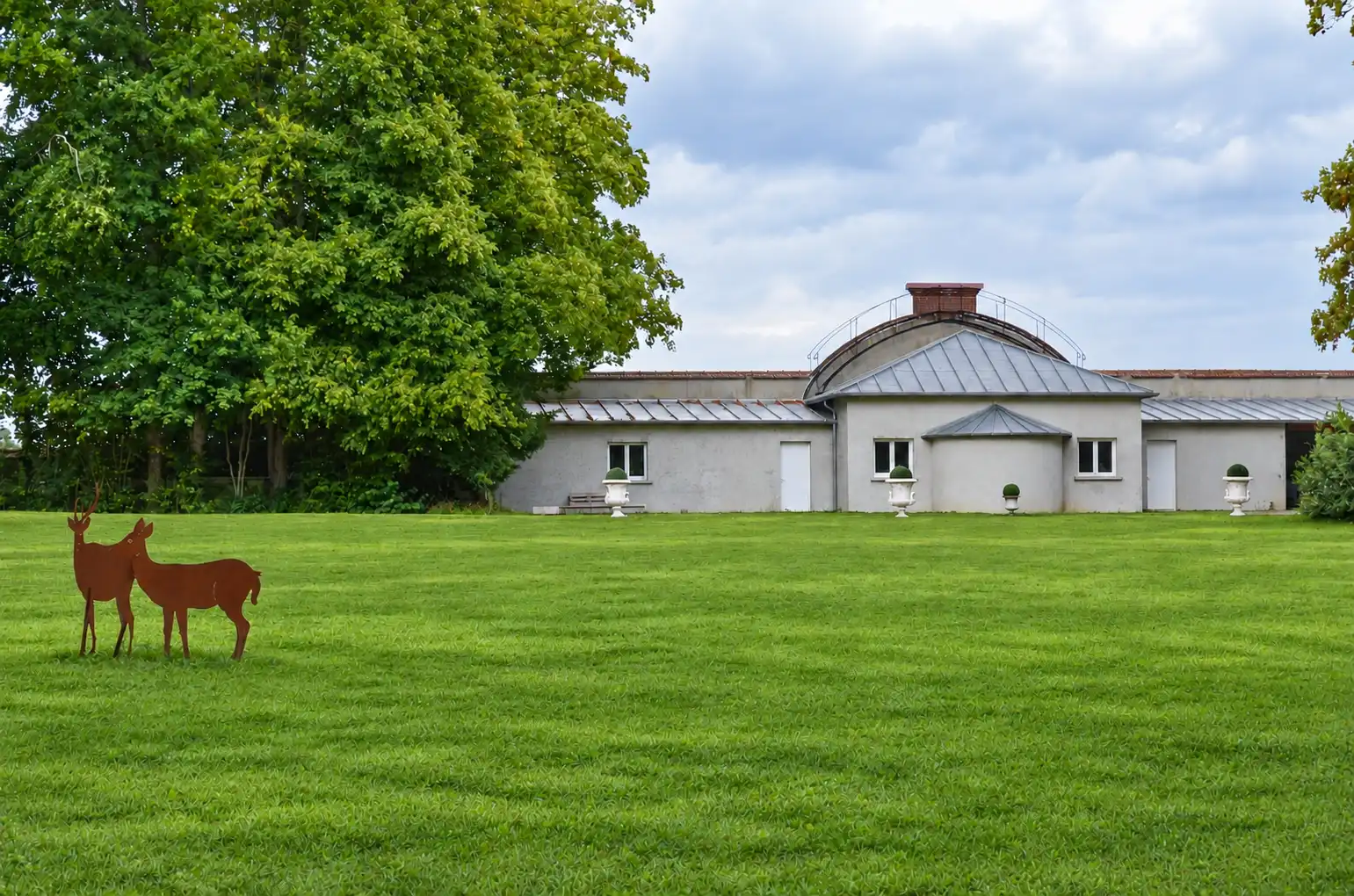 Silhouettes de cerfs en métal devant un bâtiment bas à toit de zinc