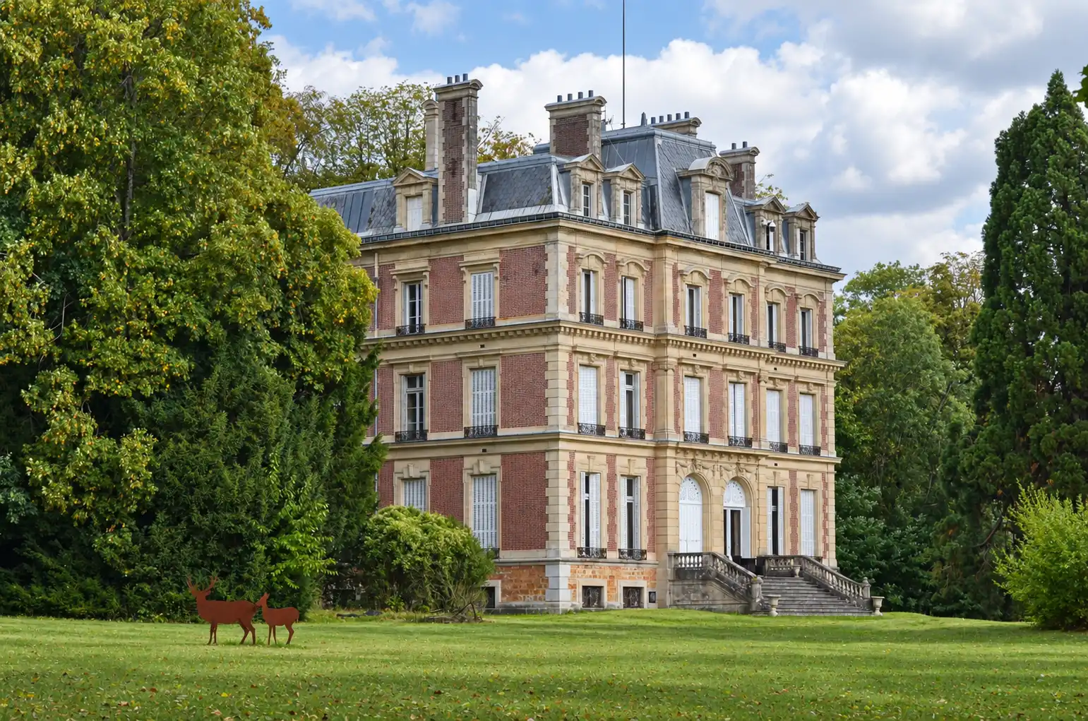 Château vu de biais avec deux silhouettes de cerfs en métal sur la pelouse