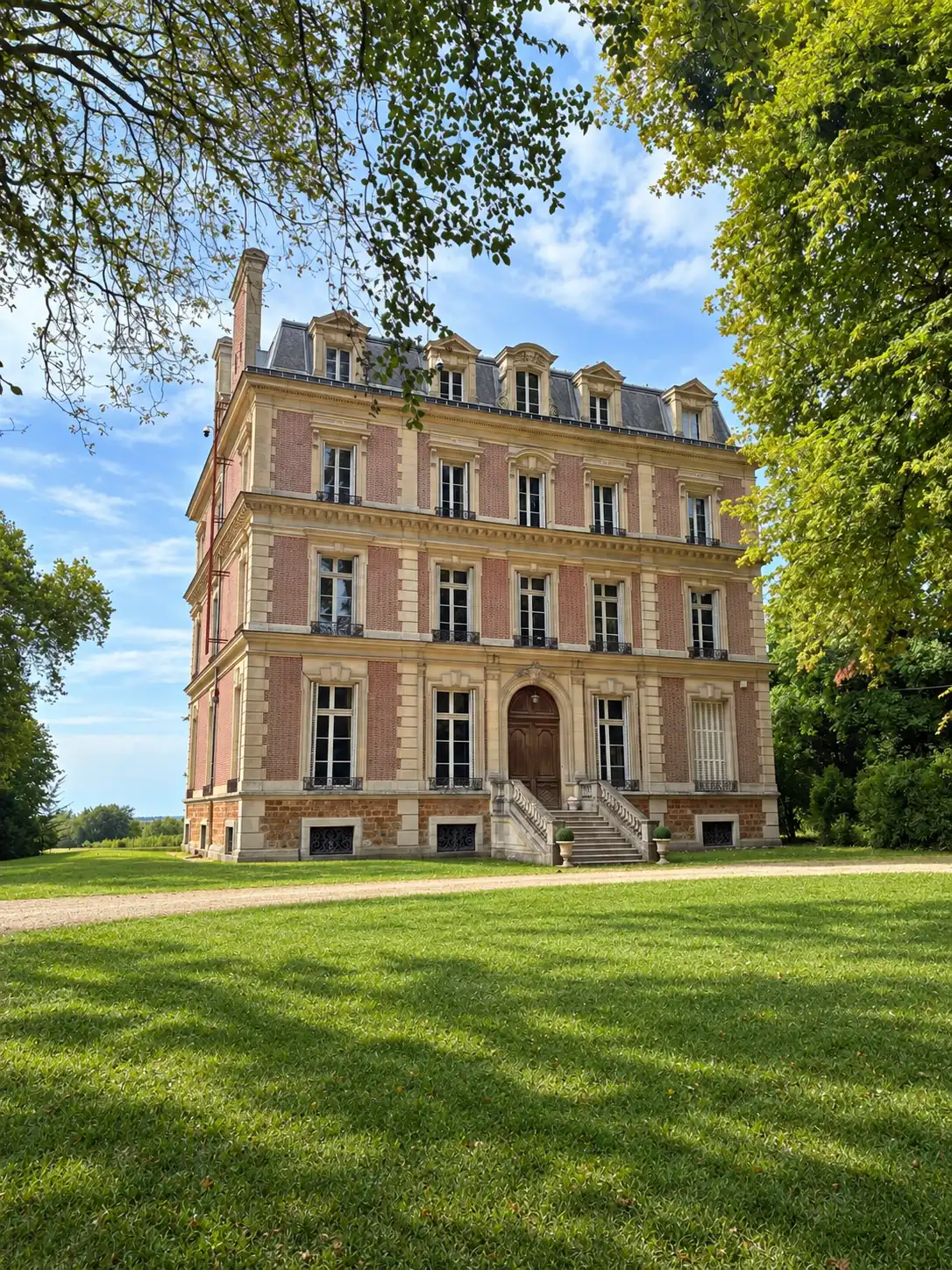 Façade en brique et pierre du château sous les arbres, escalier à double volée