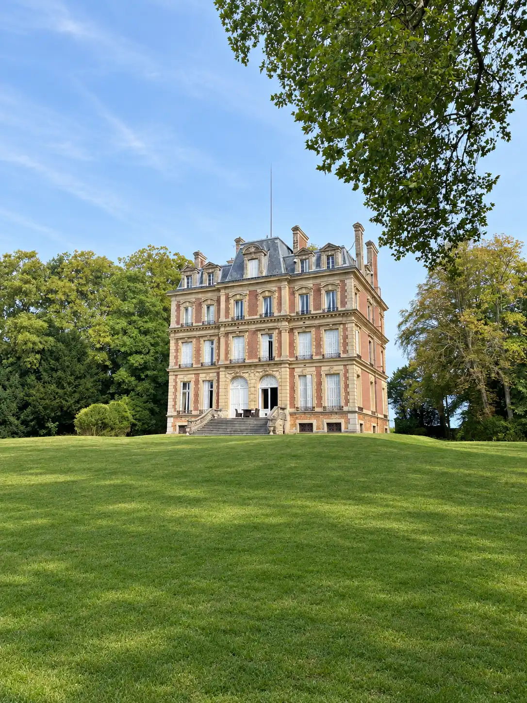 Château de trois étages au bout d'une vaste pelouse, ciel bleu