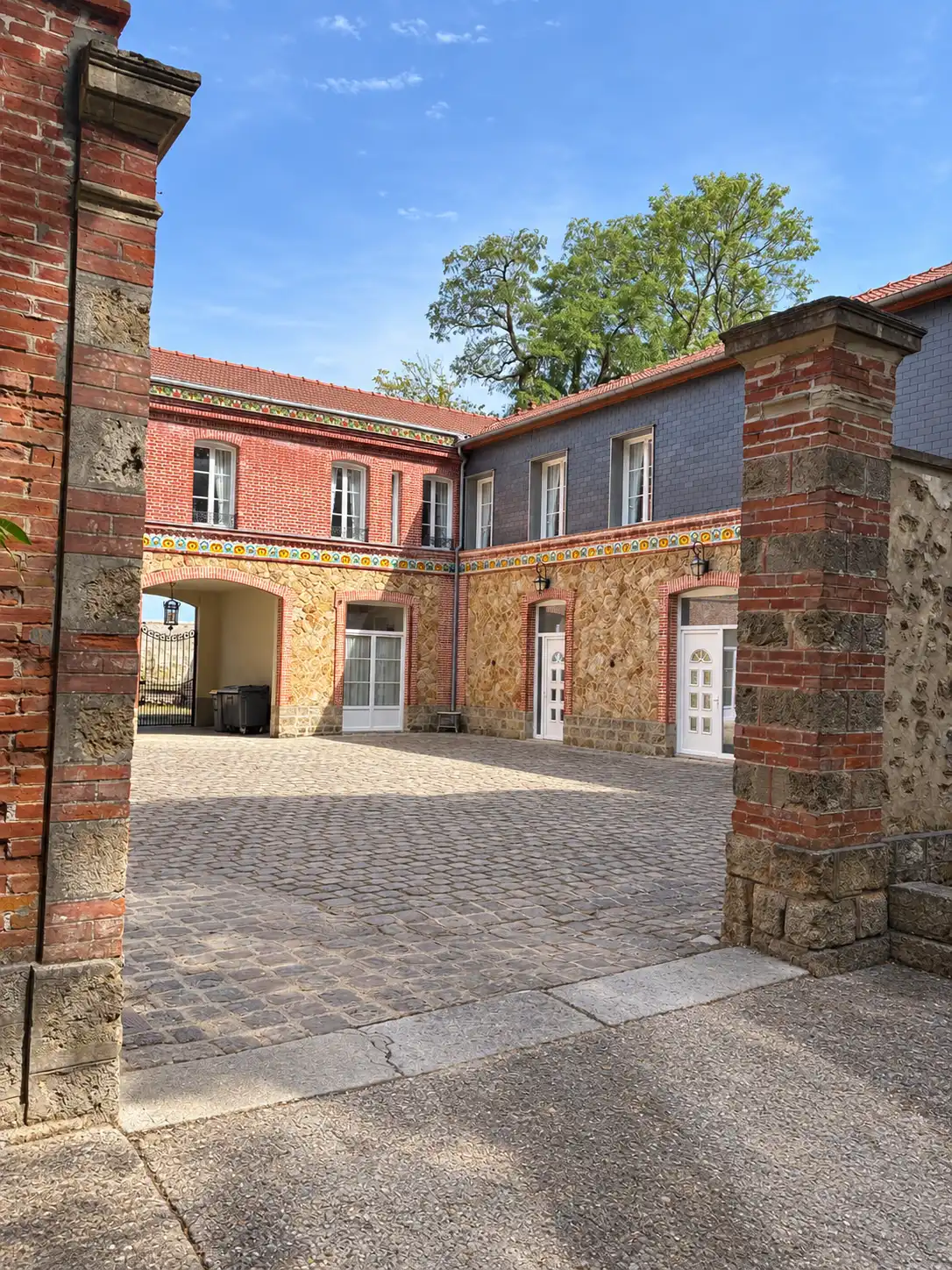 Cour pavée encadrée de piliers en brique, bâtiments en pierre et brique